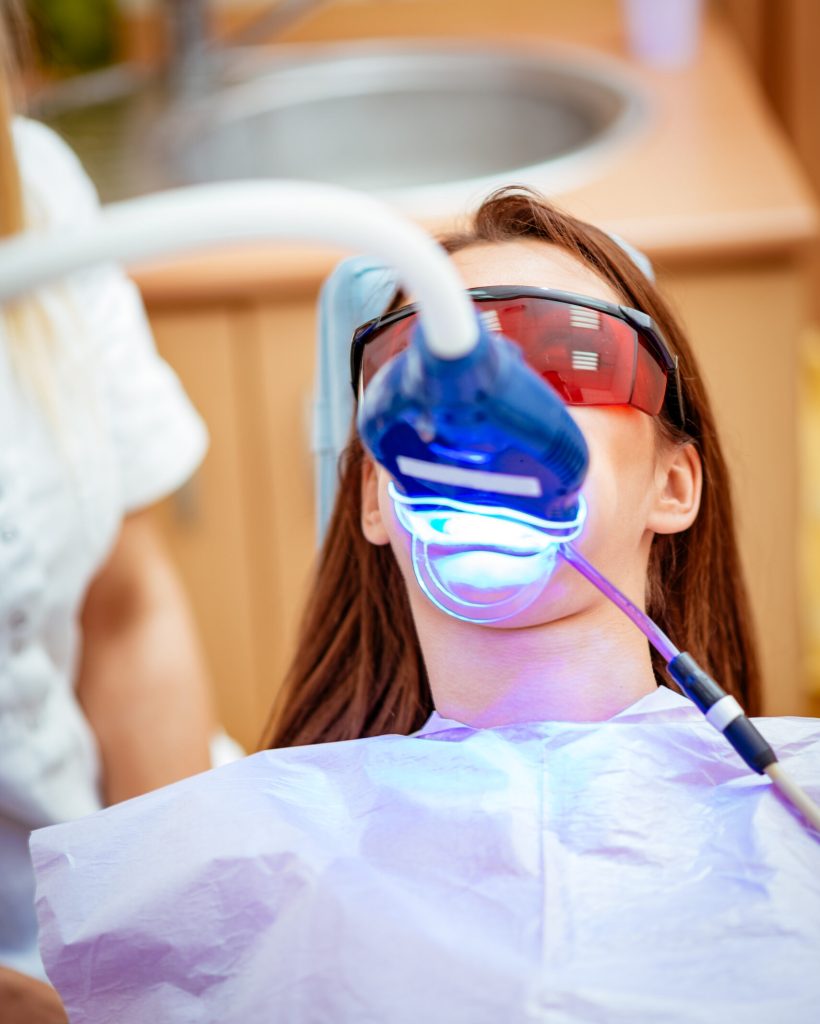 Beautiful young woman in visit at the dentist office, whitening teeth with ultraviolet light.